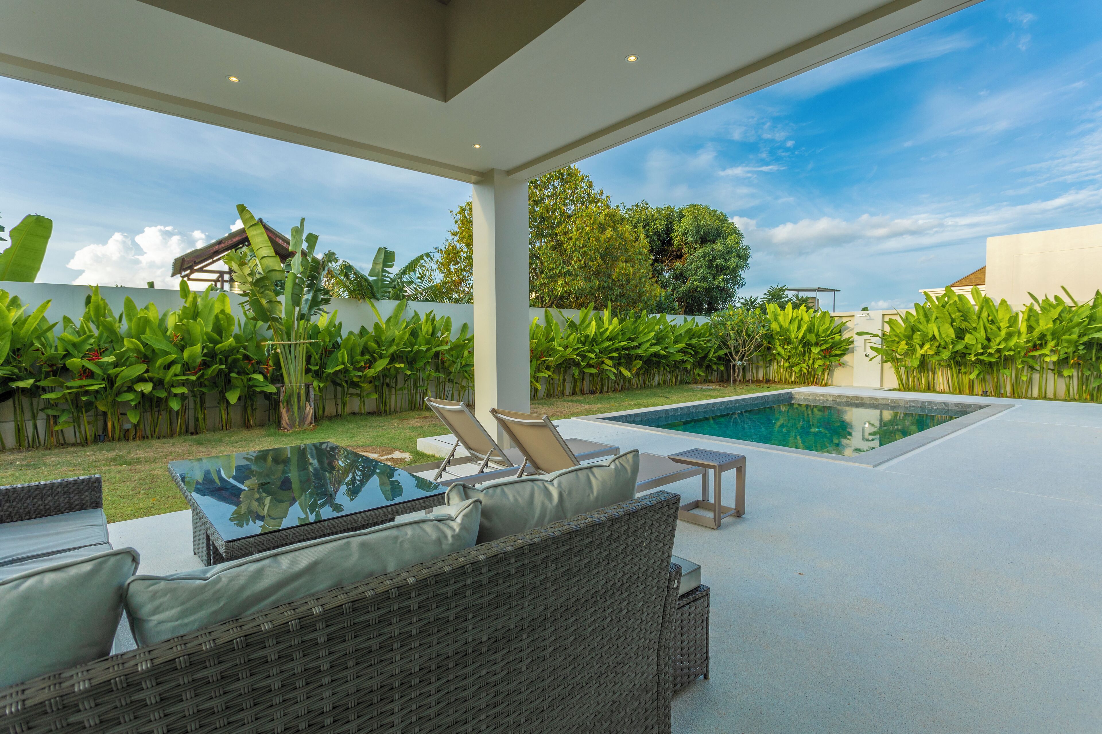 Une terrasse extérieure moderne, dotée d’une piscine, de meubles en osier et d’une végétation luxuriante.