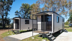 A mobile home with a covered porch and a small deck, surrounded by trees. - Tamworth Holiday Park (Hillvue)