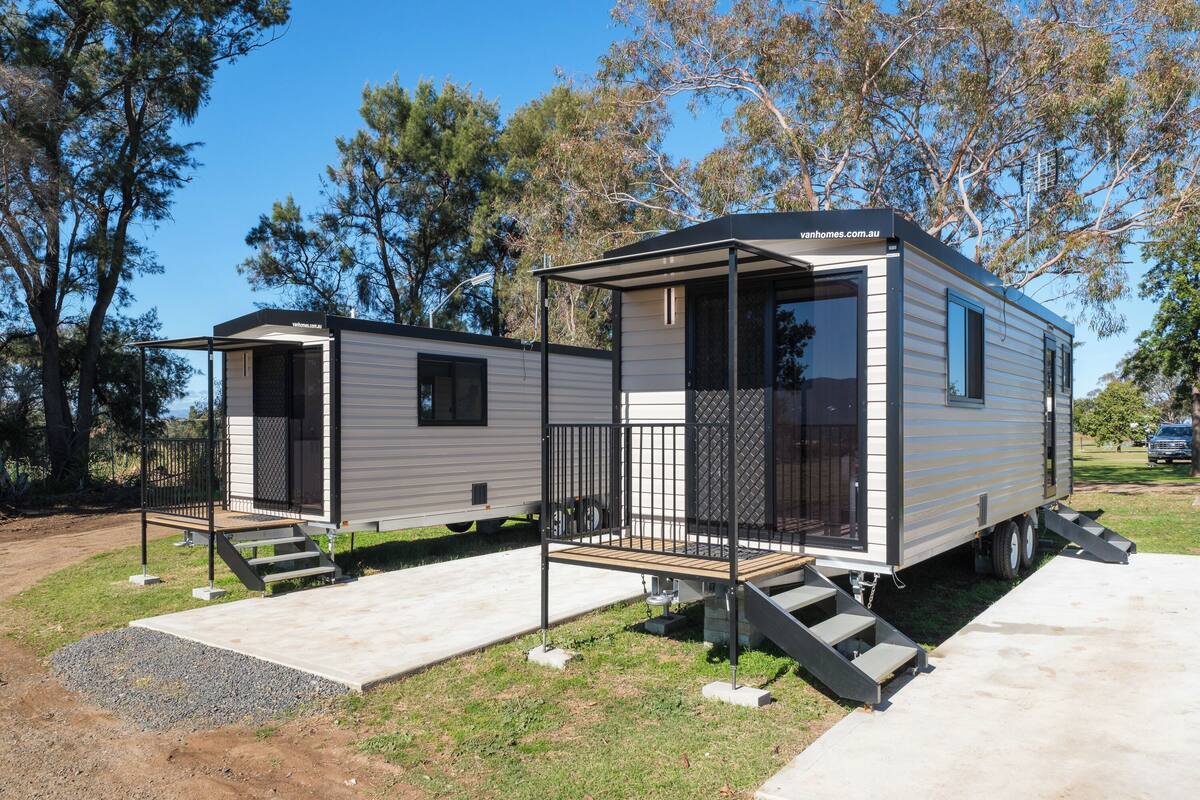 A mobile home with a covered porch and a small deck, surrounded by trees.