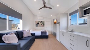 A modern, compact living space with a kitchenette, a sofa, a bed, and a ceiling fan. - Tamworth Holiday Park (Hillvue)