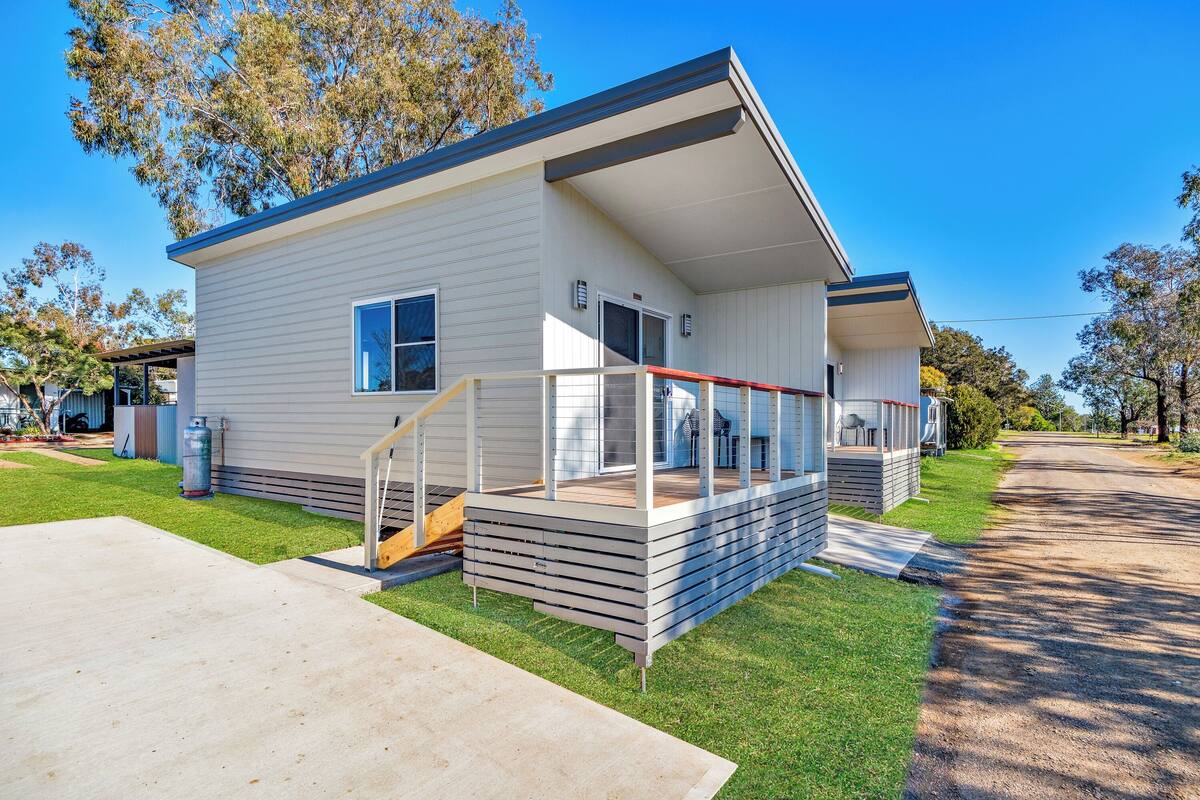A single-story mobile home with a covered porch, a small deck, and a front yard.