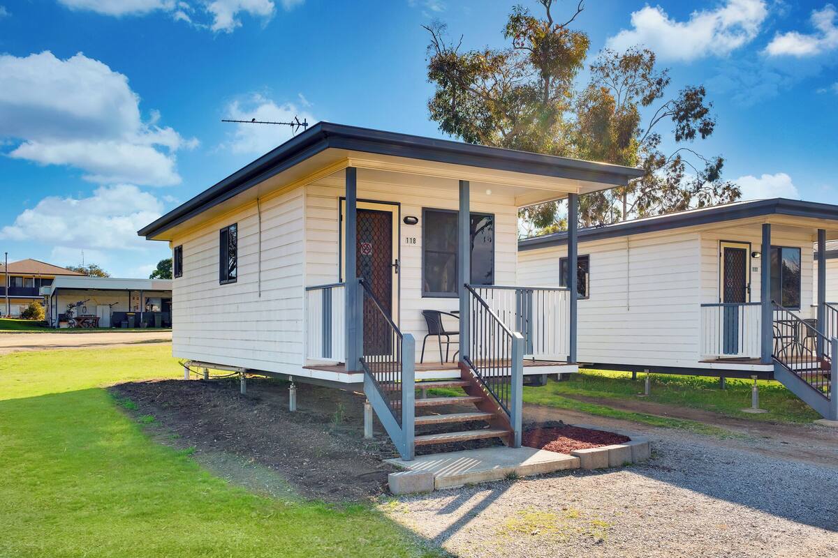 A single-story mobile home with a covered porch, a staircase, and a small front yard.