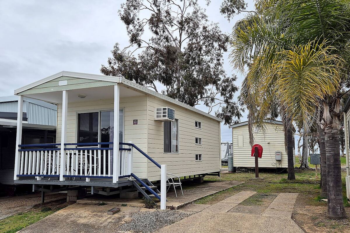 A mobile home with a porch and steps, surrounded by trees and a gravel path.