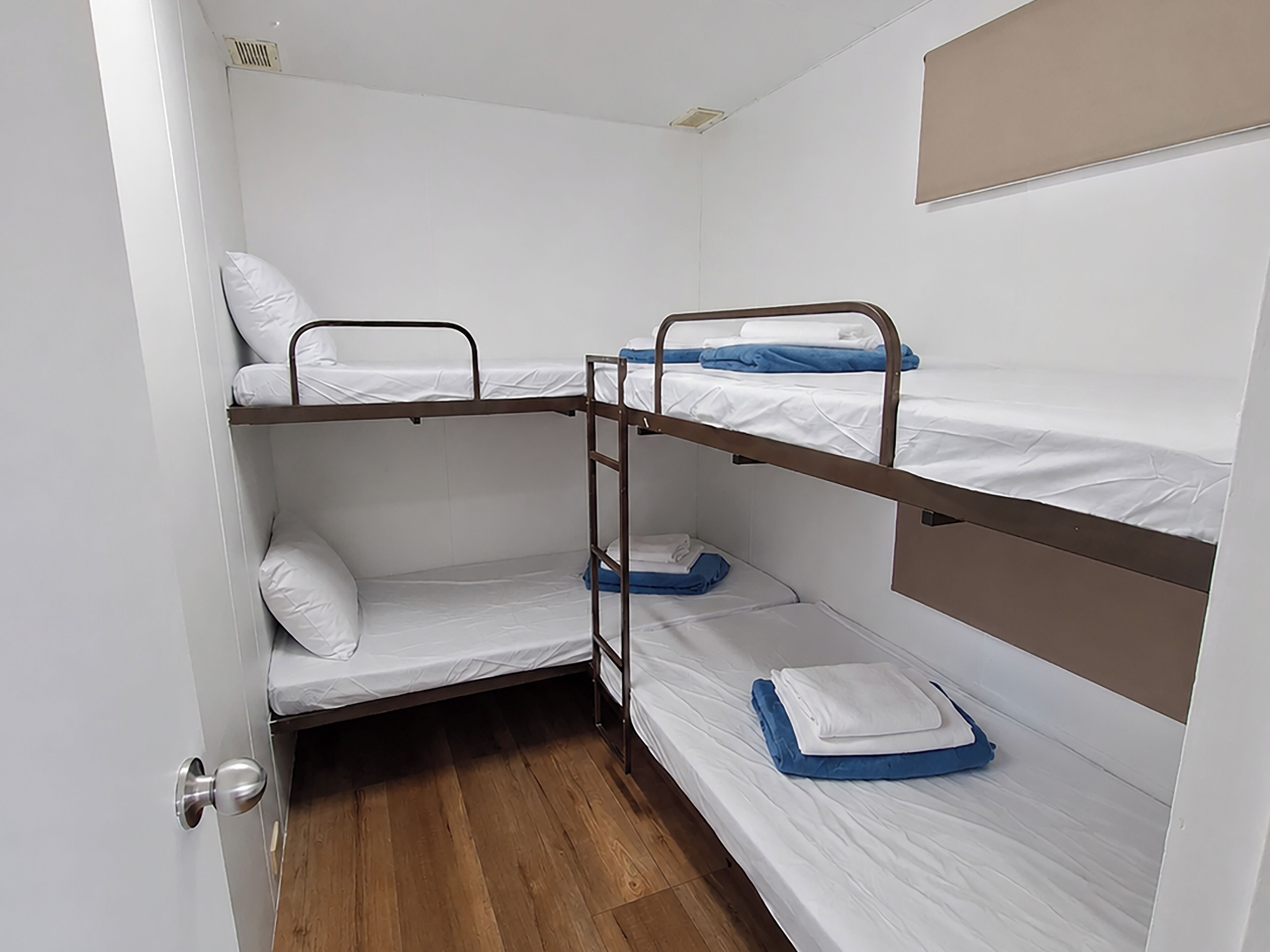 A bunk bed room with a wooden floor, a door with a silver handle, and a white wall with a vent.