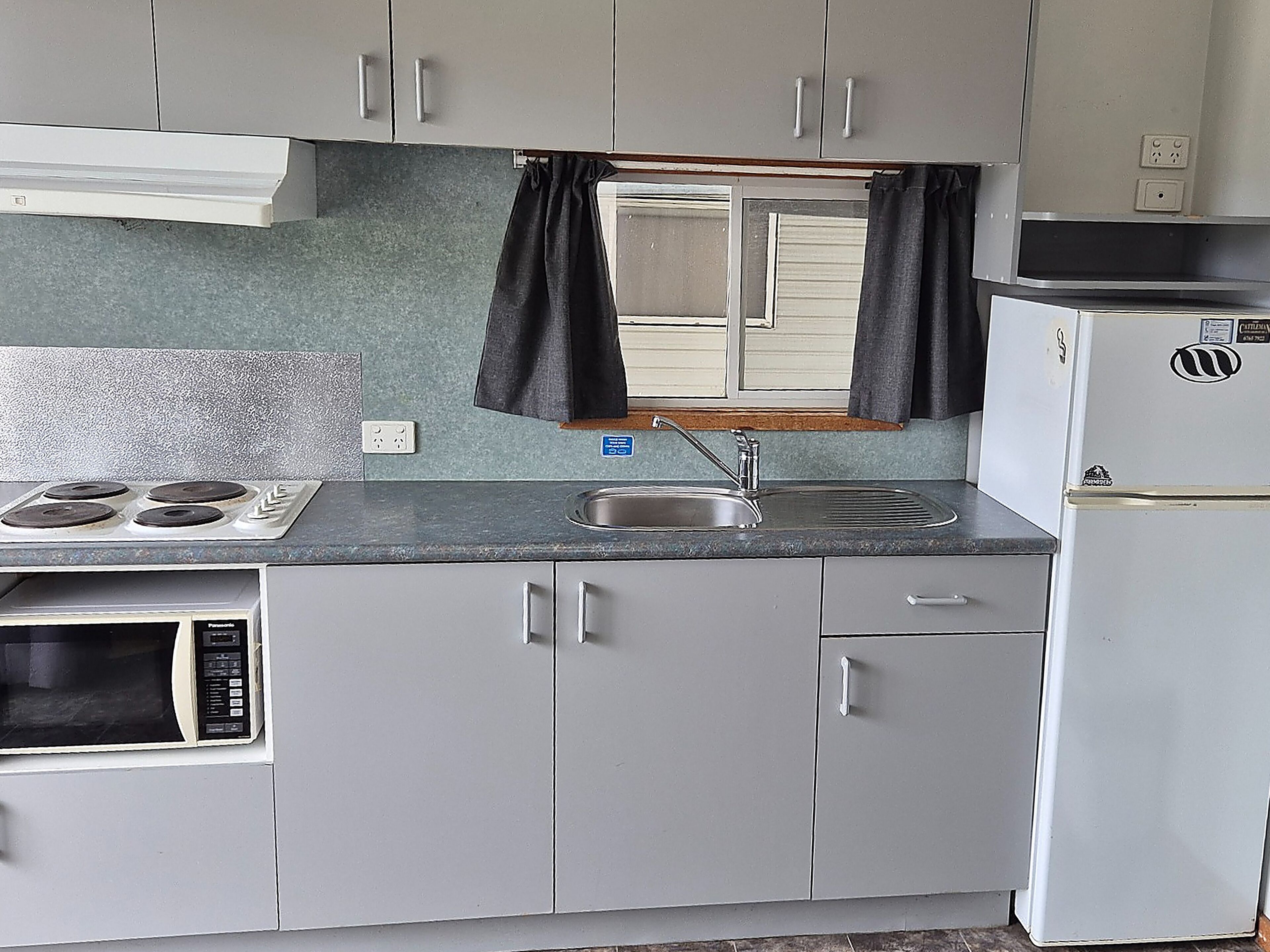 A compact kitchenette with a stove, microwave, sink, and refrigerator.