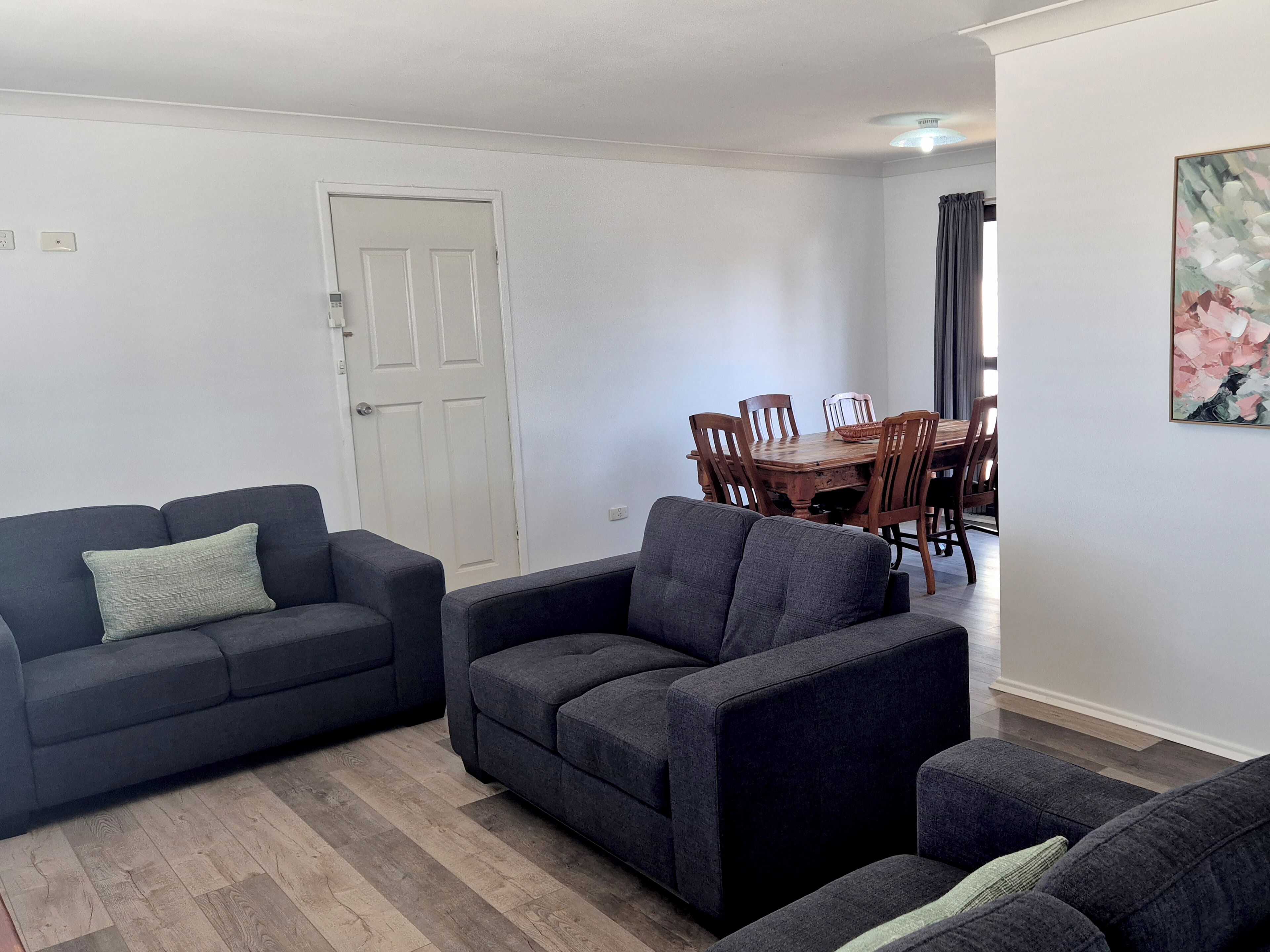 A living room with a dark grey sofa, a wooden dining table with chairs, and a white door.