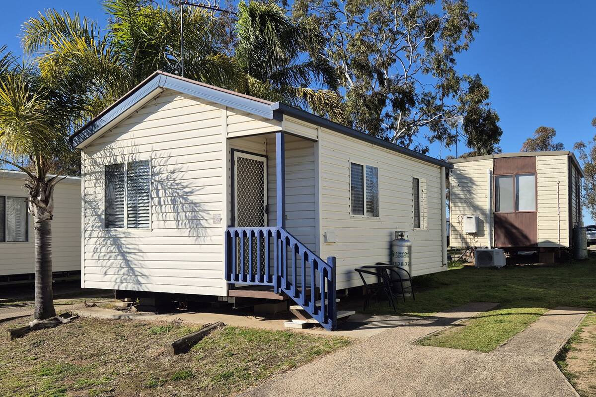 A mobile home with a porch and a small deck, surrounded by grass and trees.
