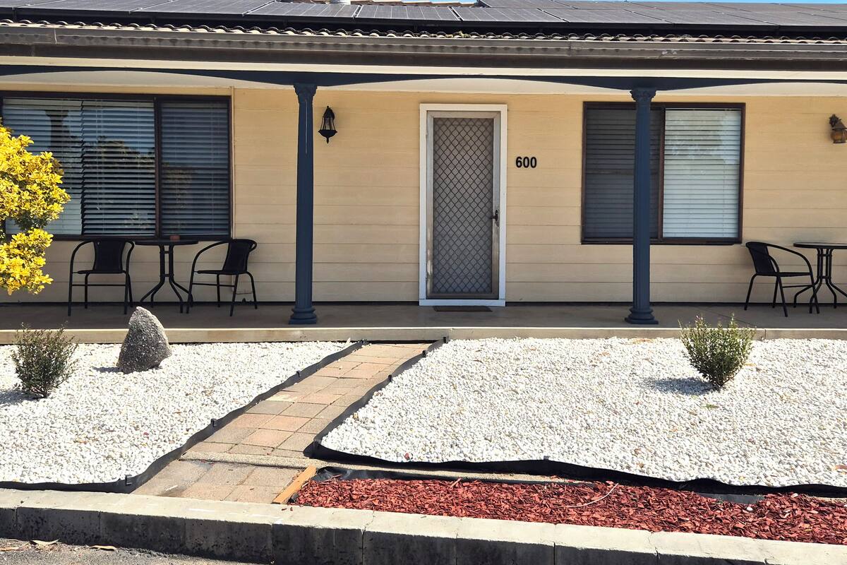 A building with a beige facade, numbered 600, featuring a covered patio with outdoor seating and a gravel pathway.