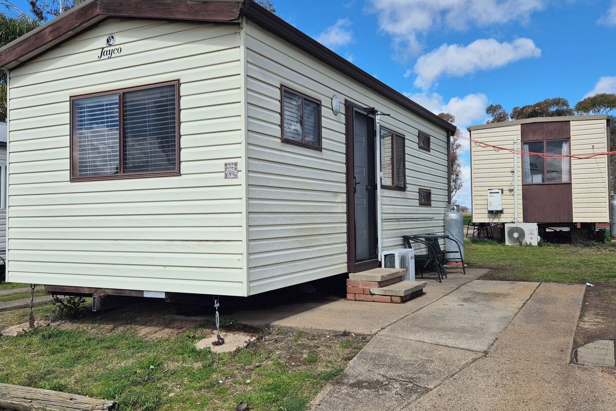 A mobile home with a dark brown roof, a small porch, and a satellite dish.