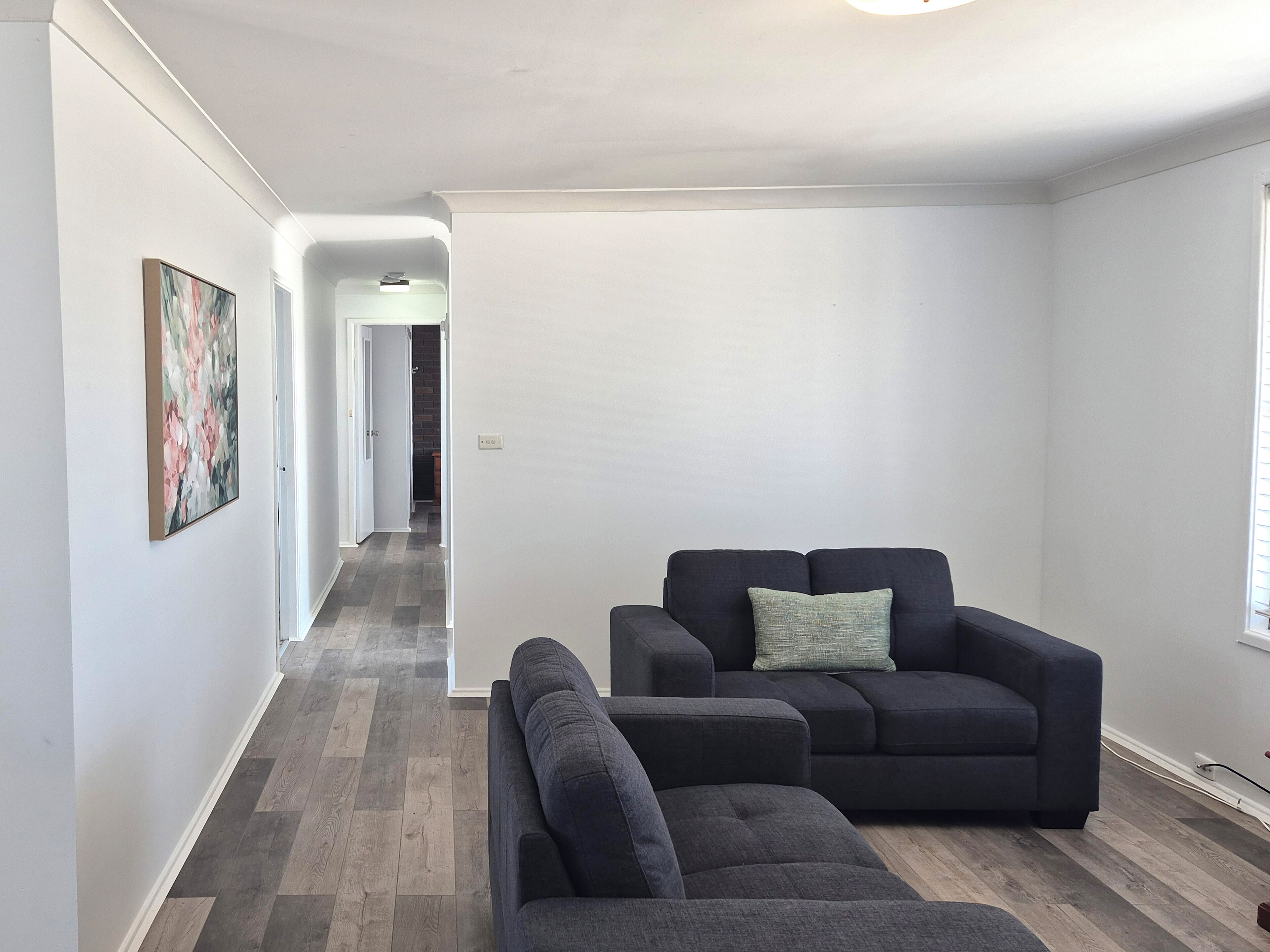 A modern living room with a dark grey sofa and a matching armchair, a small side table, and a painting on the wall.