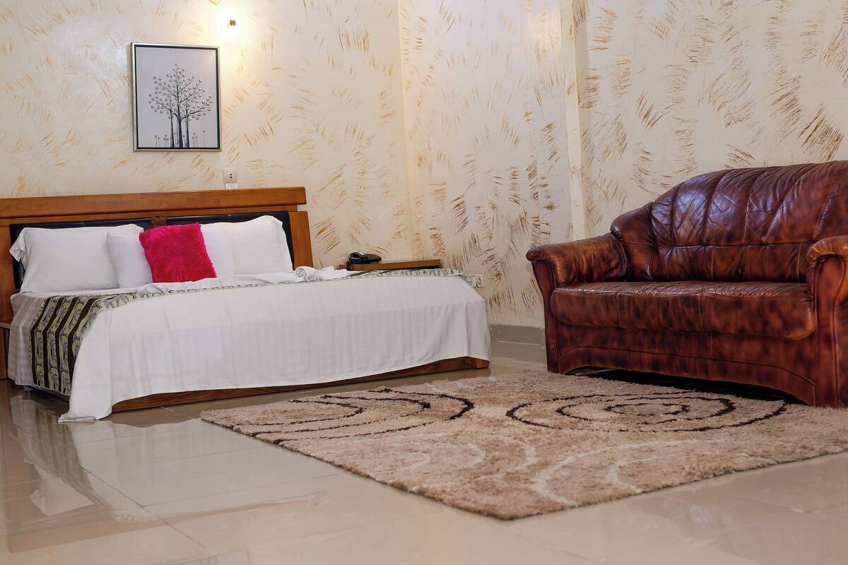 A bedroom with a bed, a brown leather chair, and a patterned rug.