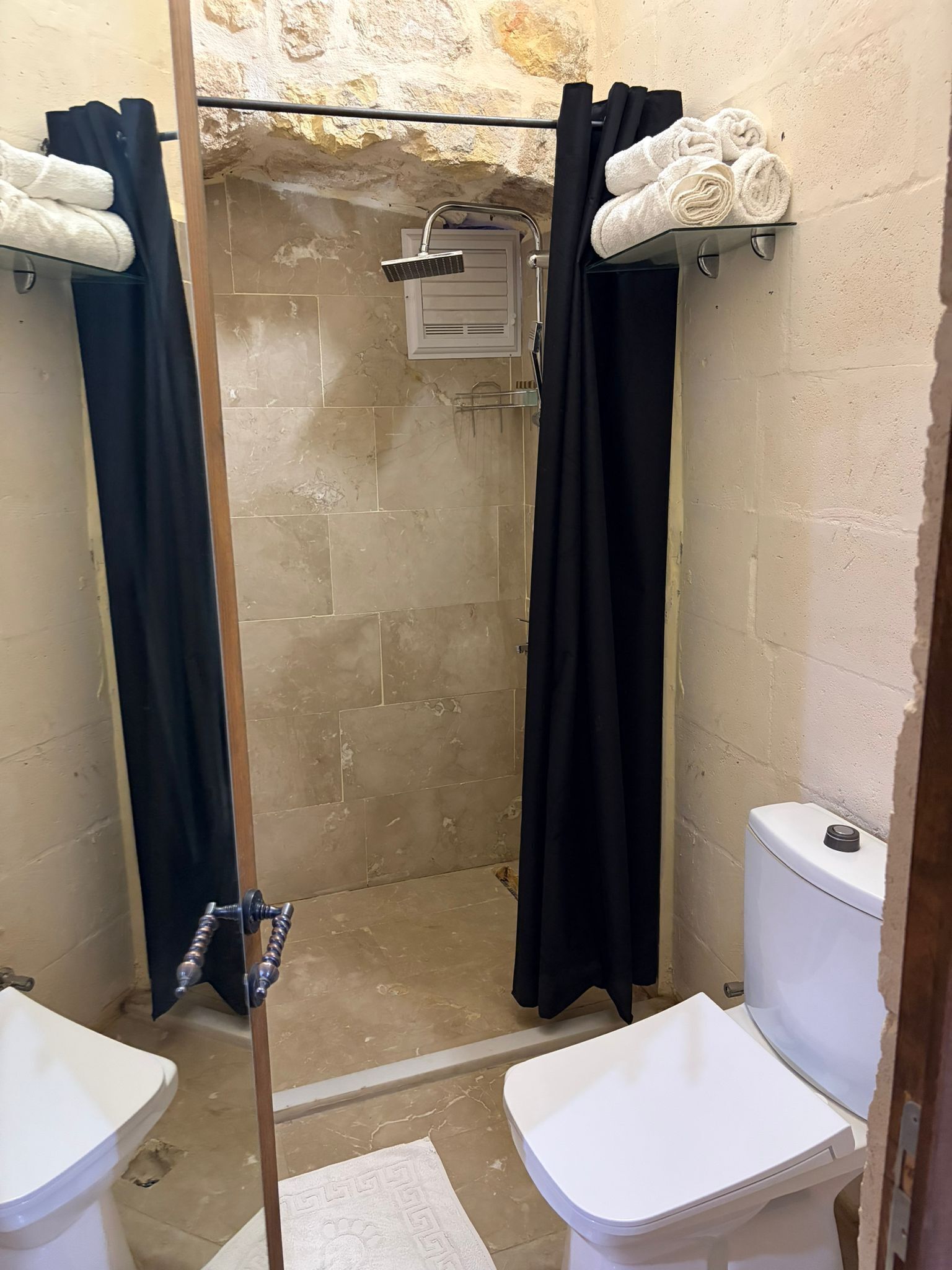 A bathroom with a shower, two toilets, and towels on racks.