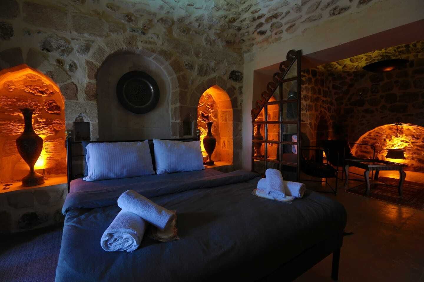 Una habitación de paredes de piedra con una cama, un florero y una chimenea.