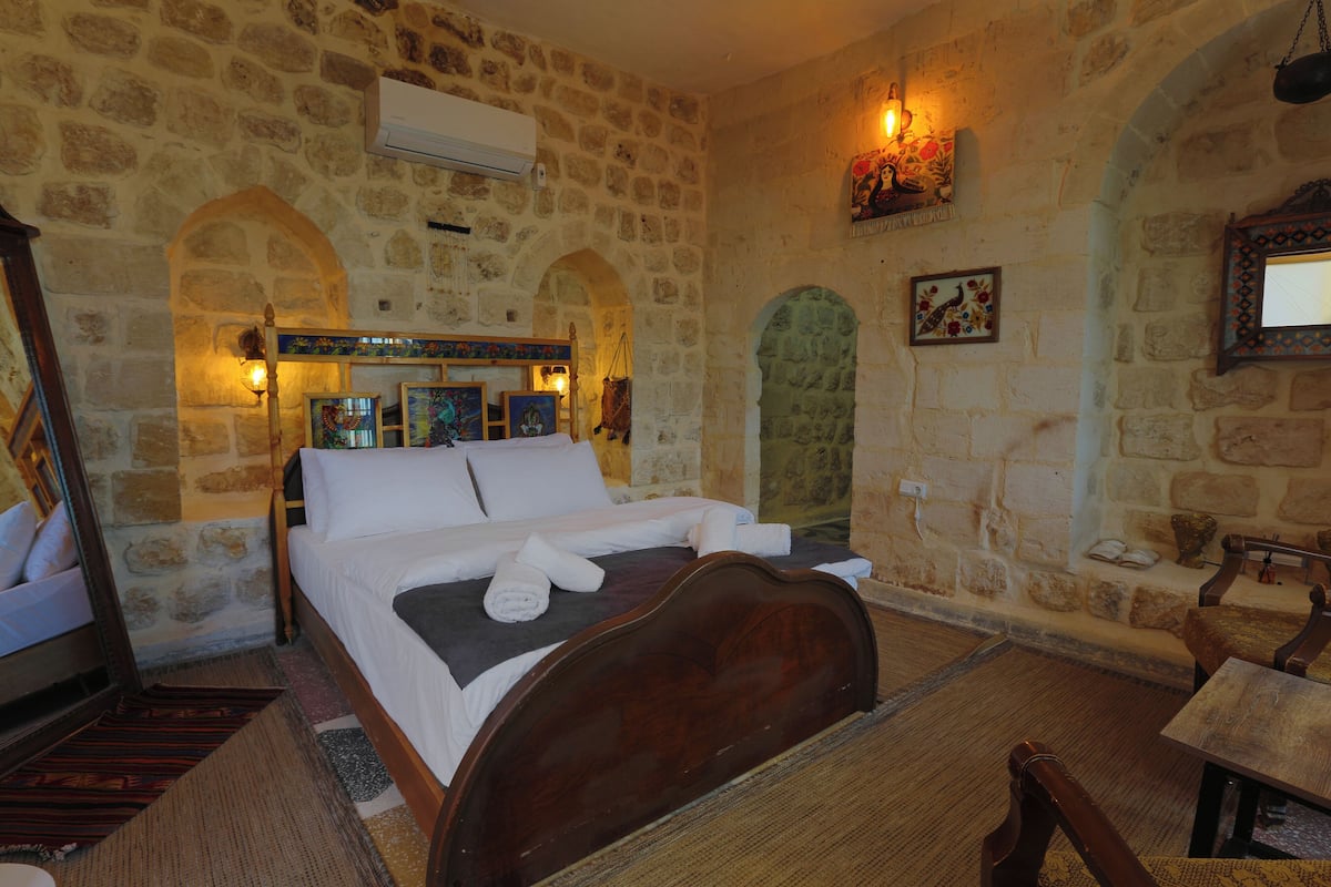 A stone-walled room with a bed, a table, and a chair.