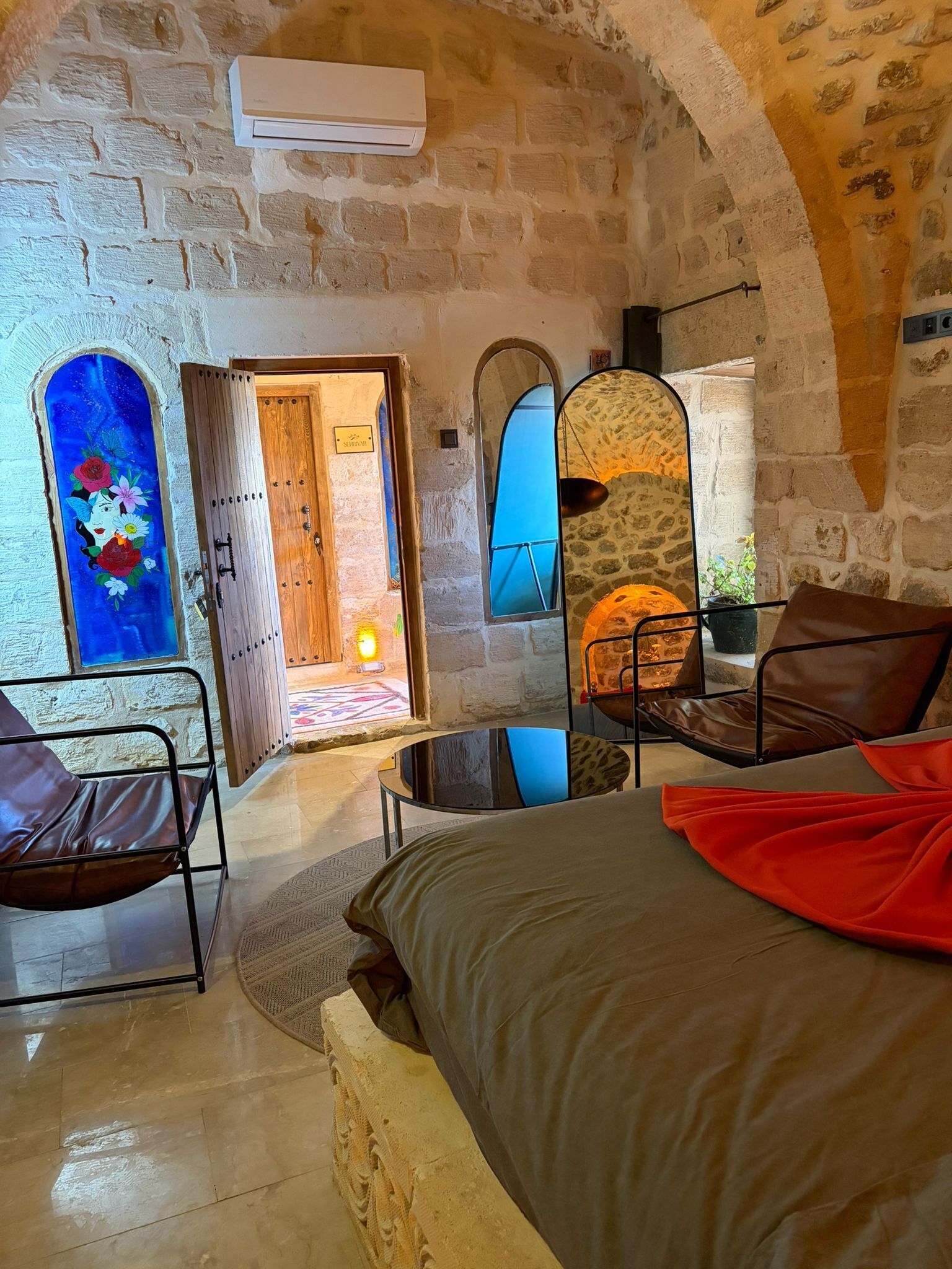 A cozy room with a bed, a chair, a table, and a mirror.