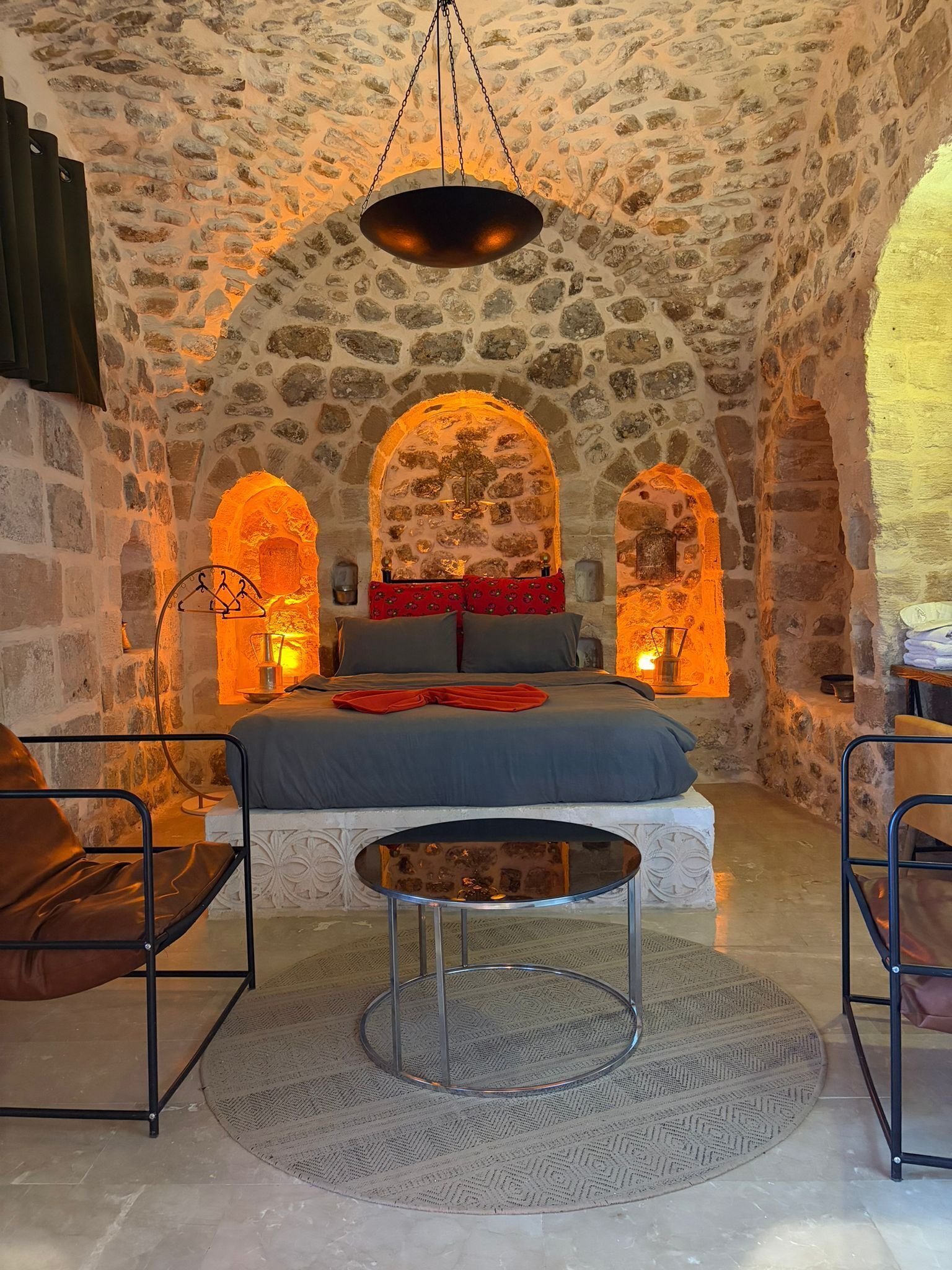 A stone-walled room with a bed, two chairs, and a round table.