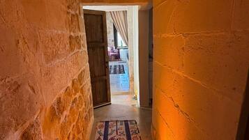 A narrow hallway with textured walls, a patterned rug, and a doorway leading to an outdoor area with a chair and table.