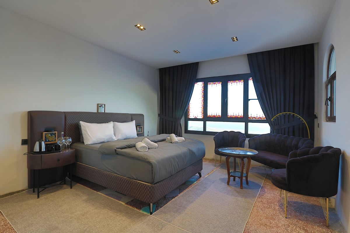 A hotel room with a bed, bedside table, lamp, and a window with curtains.