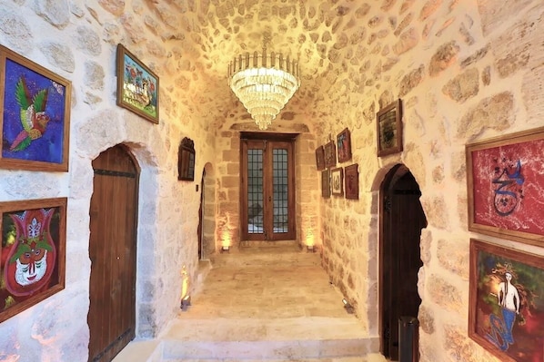 Un pasillo de paredes de piedra con un candelabro, puertas de madera y cuadros enmarcados.