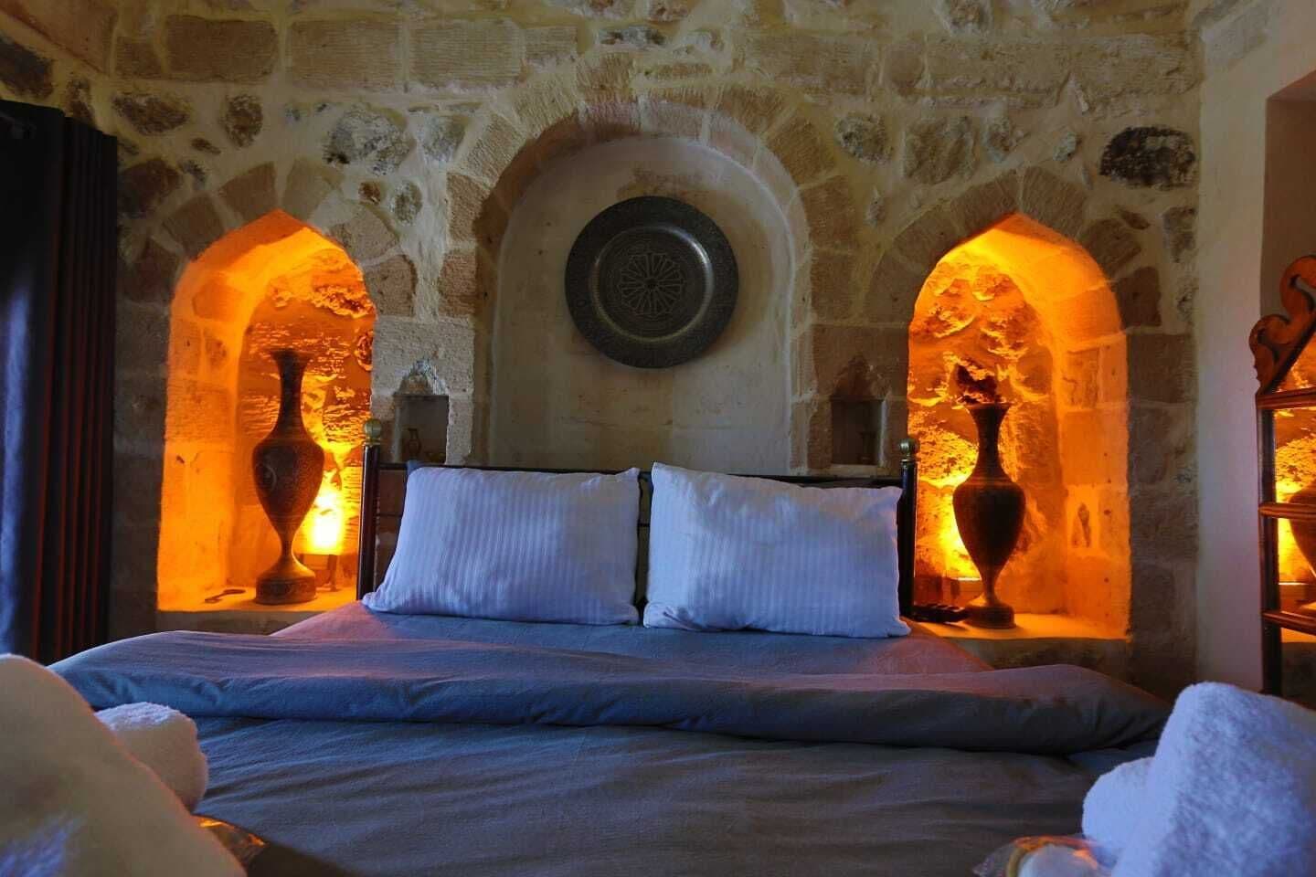 Habitación con paredes de piedra, una cama, dos jarrones y un emblema circular en la pared.