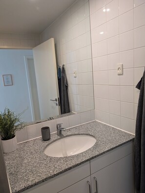 A bathroom with a granite countertop sink, white tiles, a potted plant, and a towel rack. - Apartment with a breathtaking view of the Limfjord (Aalborg)