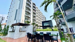 Un moderno edificio de apartamentos con varios balcones, una zona de patio con mobiliario exterior y un muro de piedra.