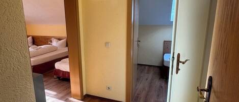 Quarto de hotel com piso de madeira, uma cama, uma porta com puxador e uma luminária no teto.