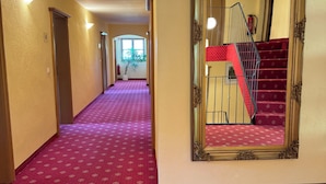 A hotel hallway with a red carpet, a staircase with red steps, and a large mirror on the wall.