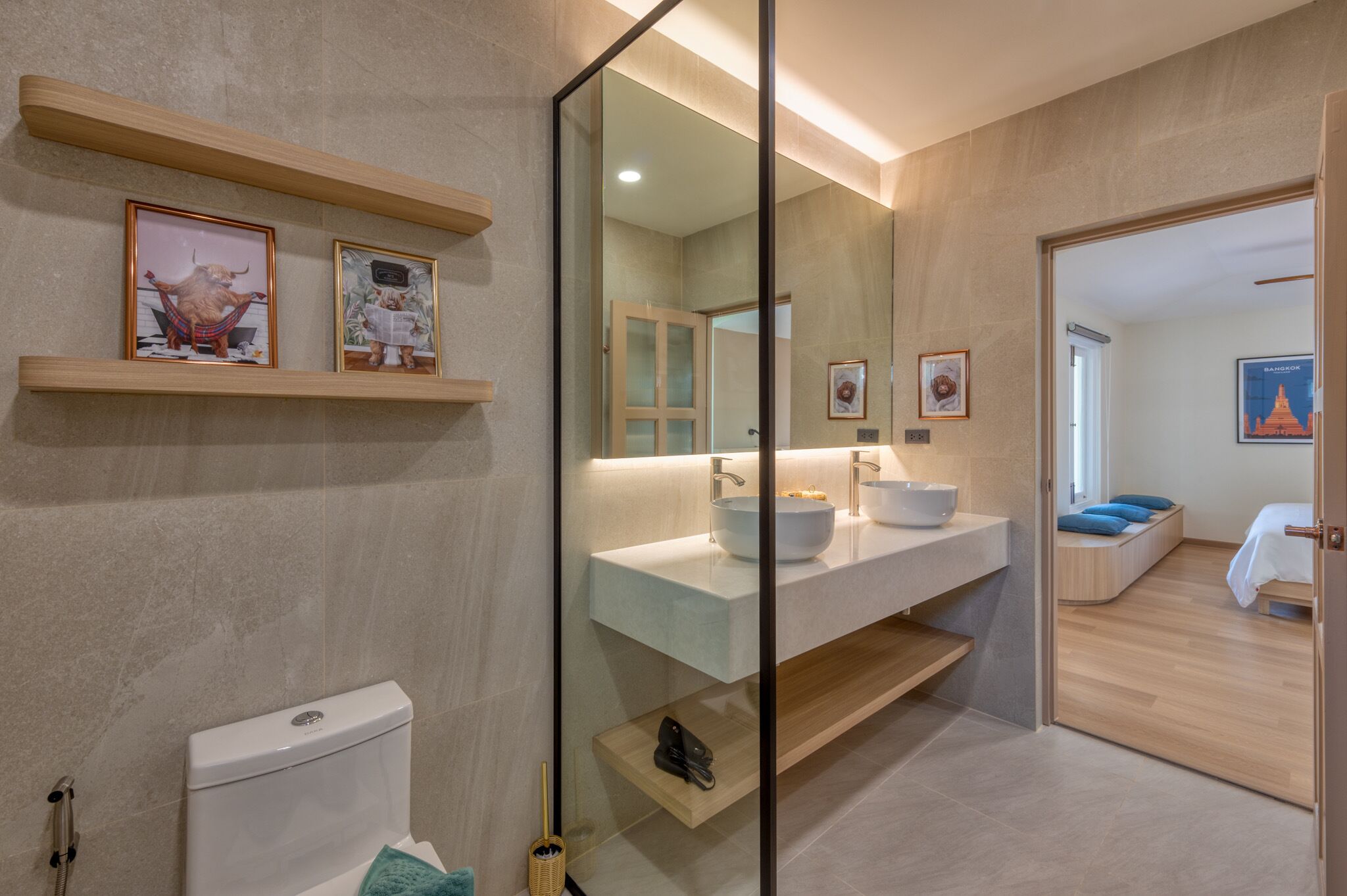 A modern bathroom with a toilet, a sink, and a mirror. There are shelves with pictures and a door leading to another room.