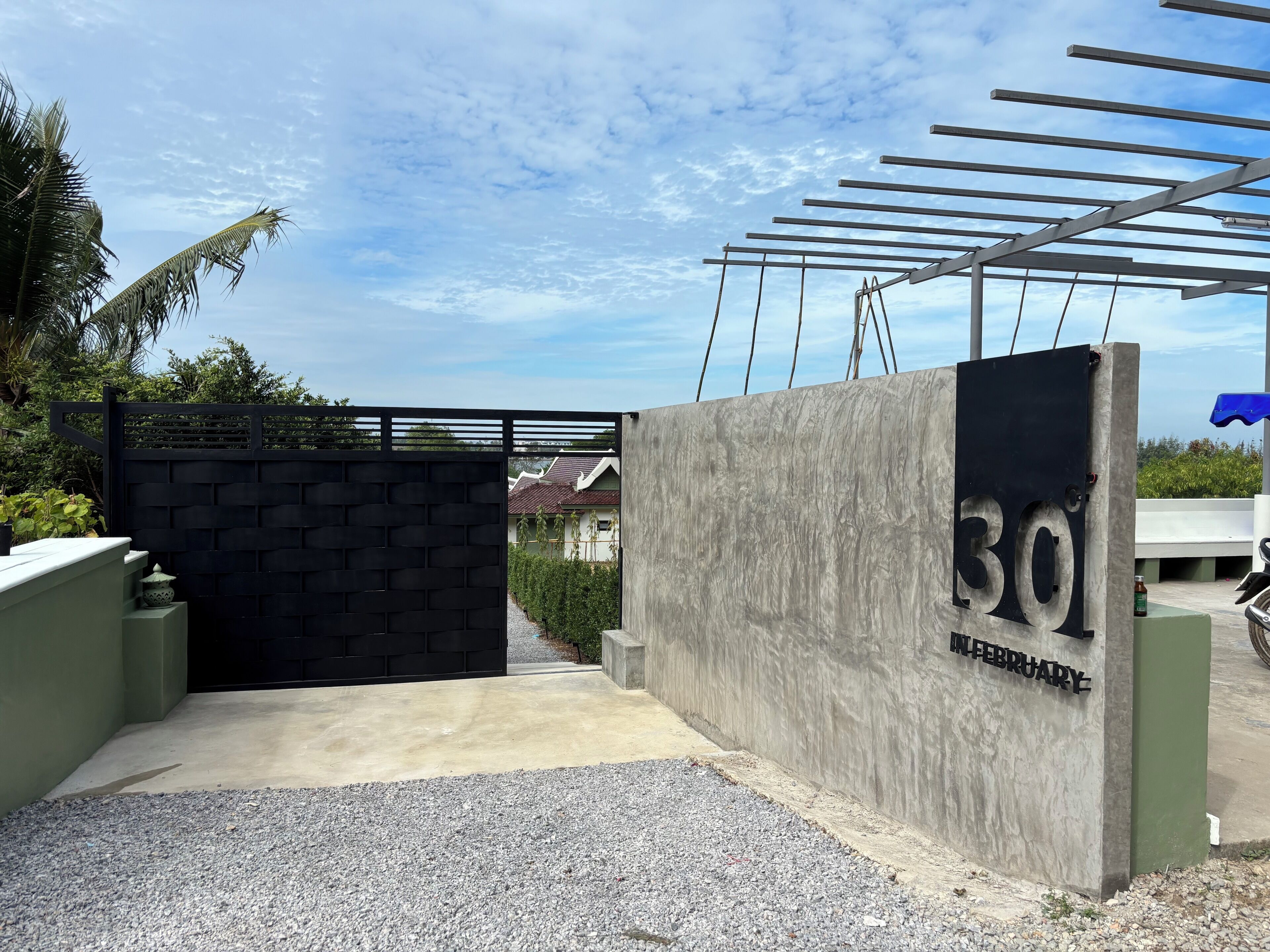 Une entrée fermée par un portail, avec un mur en béton et un portail en métal, une plaque indiquant le numéro 30 et une autre indiquant la date : février.