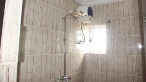 A bathroom with marble walls, a showerhead, and a window. - De Milton Hotel and Suites (Uyo)