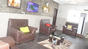 A lobby with leather sofas, a flat-screen TV, a ceiling fan, and a patterned rug. - De Milton Hotel and Suites (Uyo)