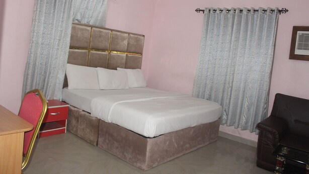 A bedroom with a bed, a desk, a chair, and curtains. - De Milton Hotel and Suites (Uyo)