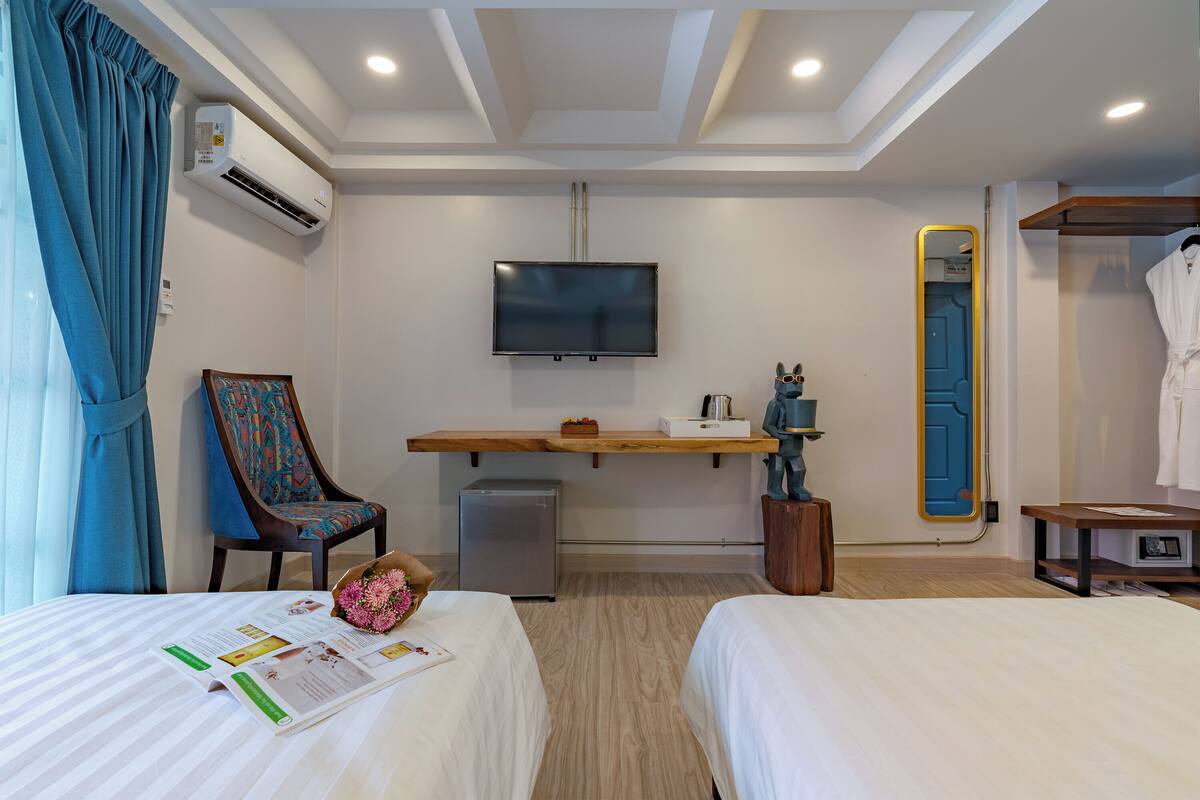 Habitación de hotel con dos camas, un escritorio, un televisor de pantalla plana, un refrigerador pequeño y un espejo.