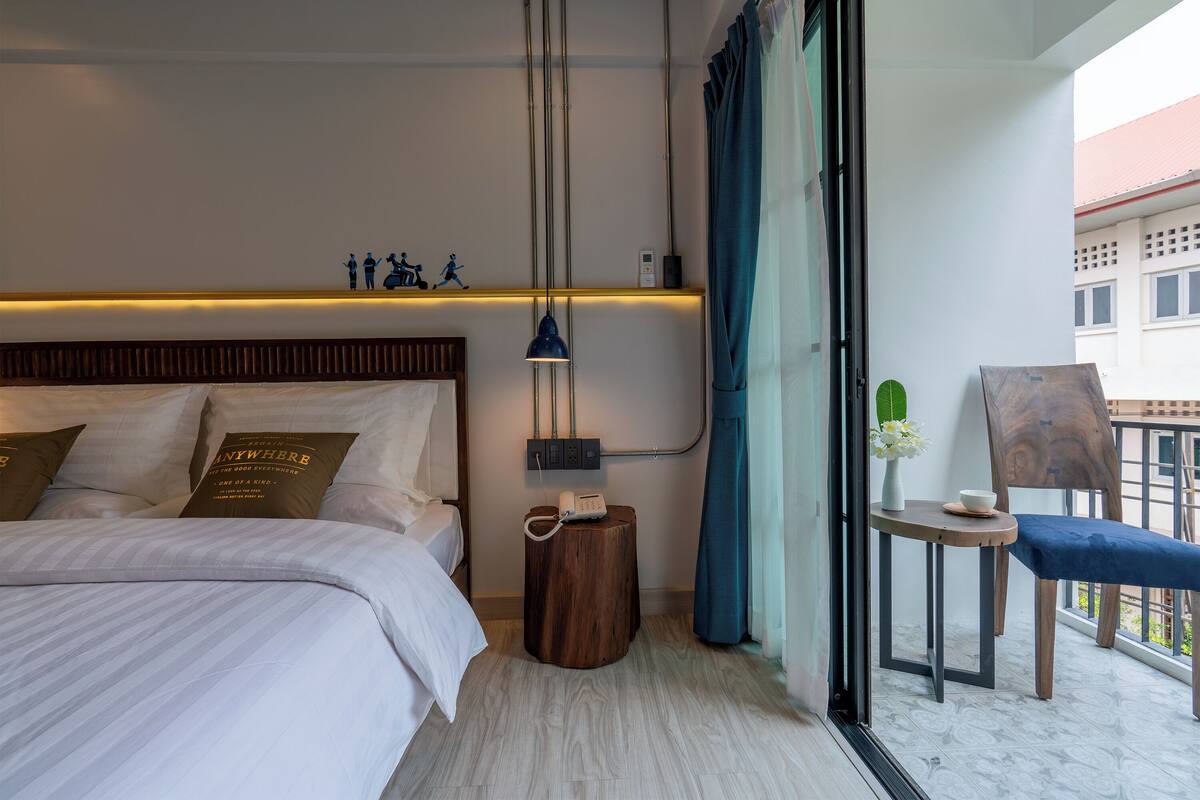 Habitación de hotel con cama, mesita de noche y un pequeño balcón con silla y mesa.
