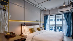 Habitación de hotel con una cama grande, una mesita de noche con frutero, un espejo y vistas de la ciudad a través de amplios ventanales.
