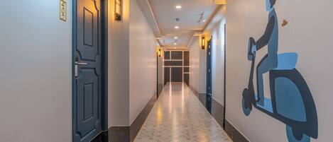 A hotel hallway with a patterned floor, a blue door, and a wall mural of a person on a scooter.