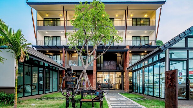 Un edificio moderno con fachada de vidrio, un árbol central y asientos al aire libre.