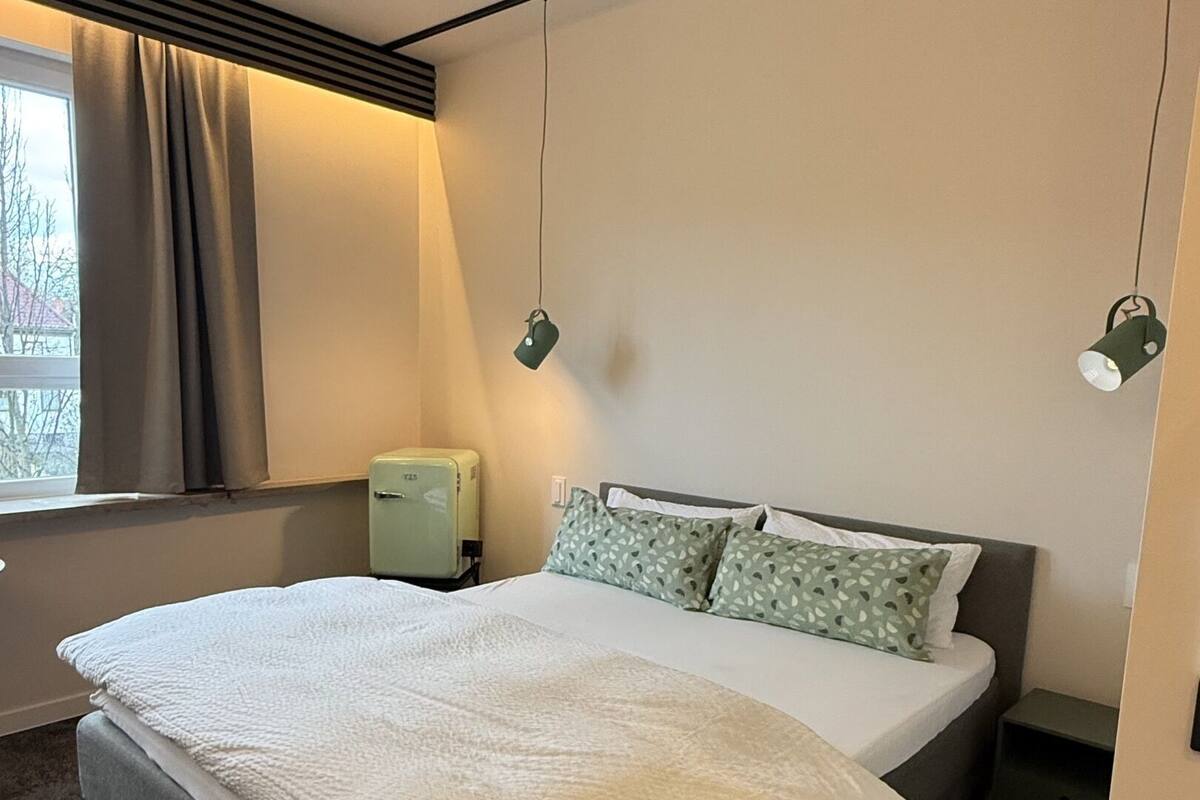 A bedroom with a bed, a nightstand, a lamp, and a window with curtains.