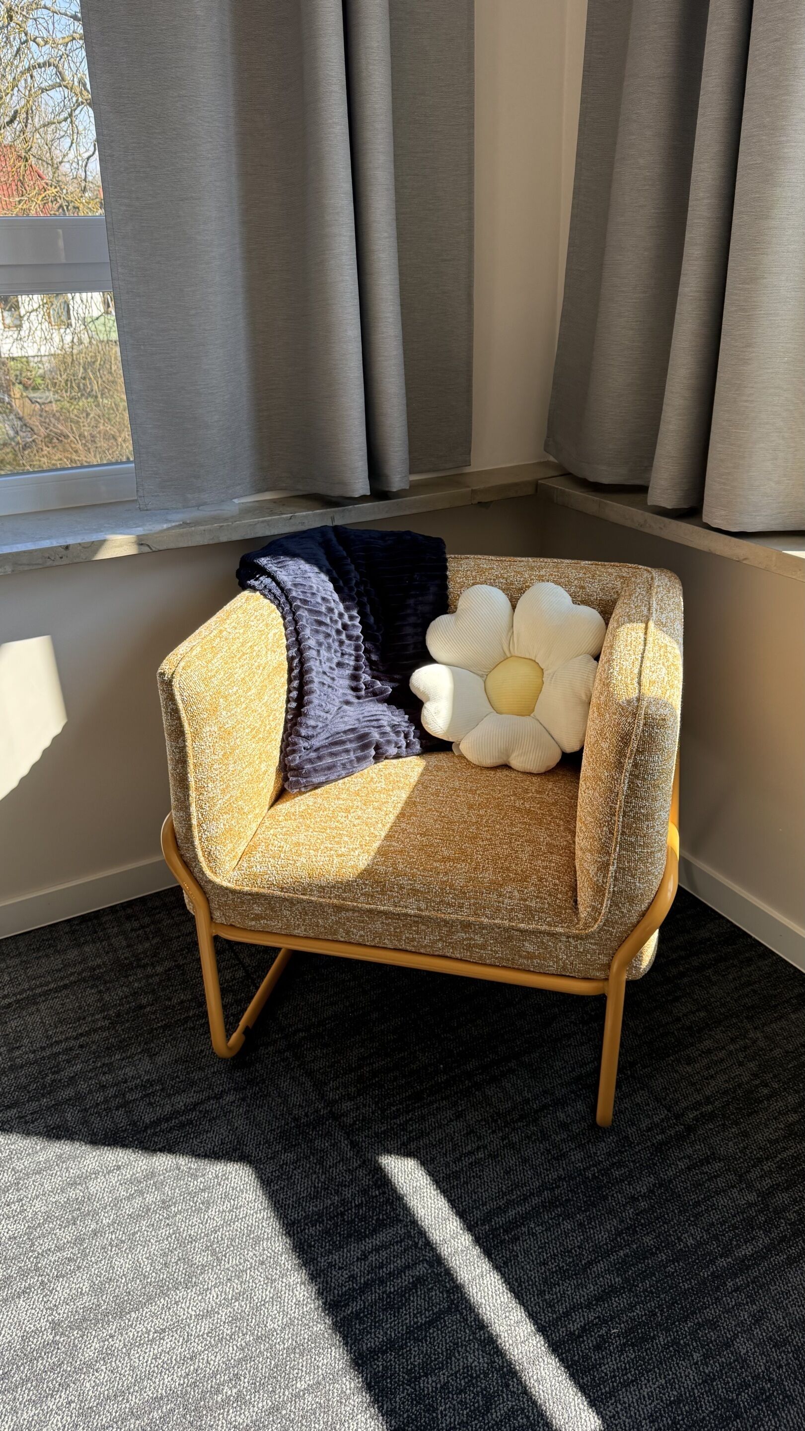 A corner seating area with a patterned sofa, a large flower-shaped pillow, and a dark throw blanket.