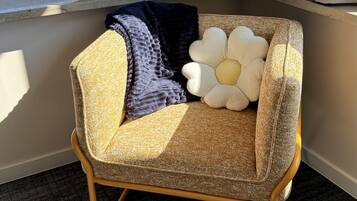 A corner seating area with a patterned sofa, a large flower-shaped pillow, and a dark throw blanket.