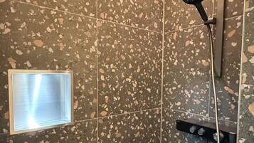 A shower with a handheld showerhead, a wall-mounted control panel, and a small window.