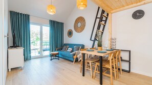 A modern living room with a blue sofa, wooden dining table, and a staircase. - Apartamenty Sun & Snow Resort Jantar (Stegna)