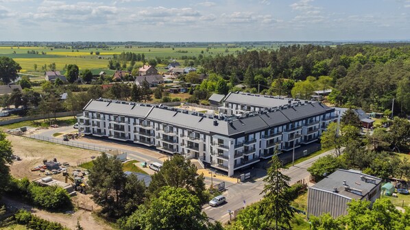 A modern multi-story building with a flat roof, surrounded by greenery and residential areas. - Apartamenty Sun & Snow Resort Jantar (Stegna)