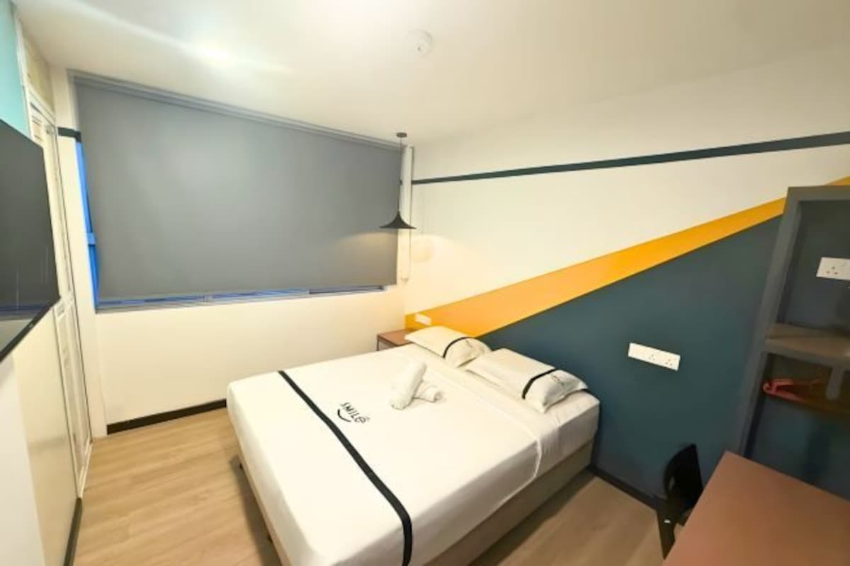 A small, neatly arranged bedroom with a single bed, a bedside table, a lamp, and a window.