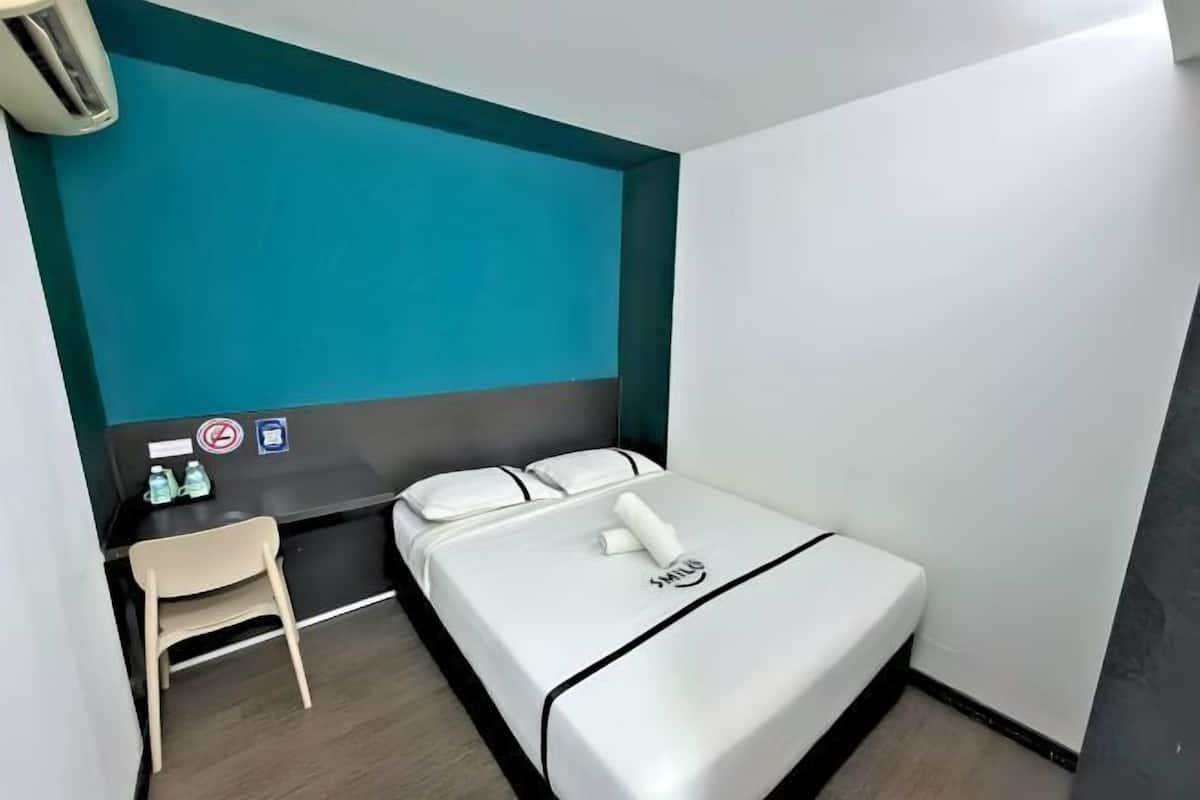 Una camera d'albergo modesta con un letto, una scrivania, una sedia e una parete azzurra.
