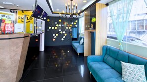A hotel lobby with a reception desk, a blue sofa, a chandelier, and a wall decorated with hexagonal shapes. - Smile Hotel SS2 Petaling Jaya (Petaling Jaya)