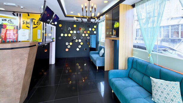 Un vestíbulo de hotel con un mostrador de recepción, un sofá azul, una araña y una pared decorada con formas hexagonales.
