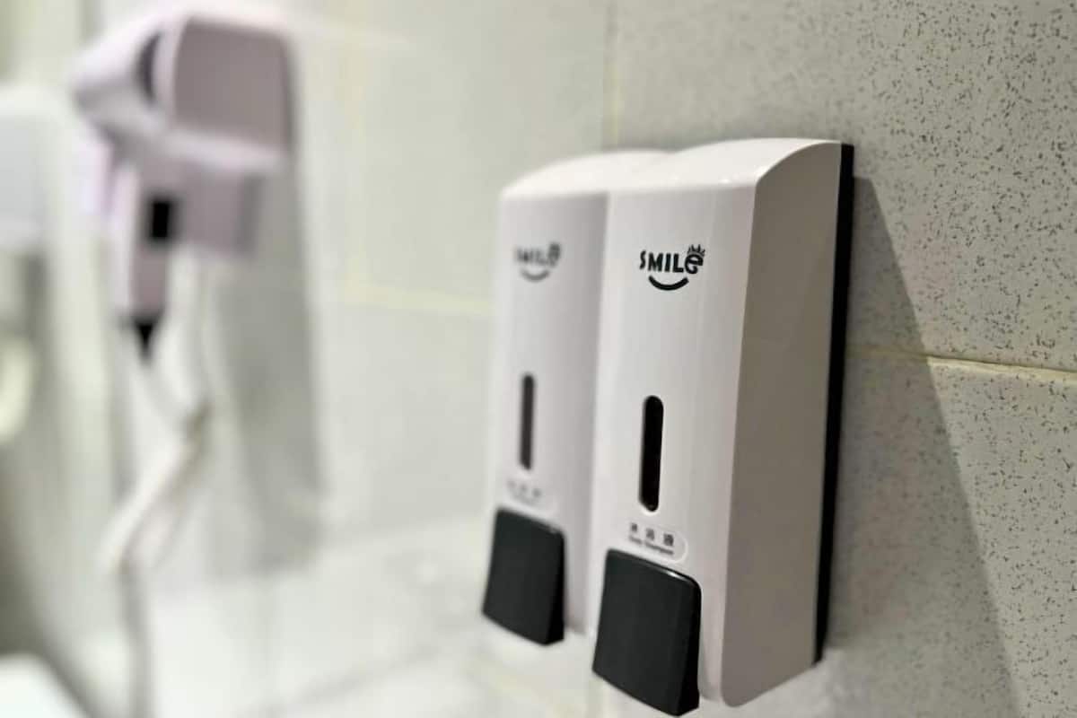 Una fila di erogatori di disinfettante per le mani fissati a una parete rivestita di piastrelle.