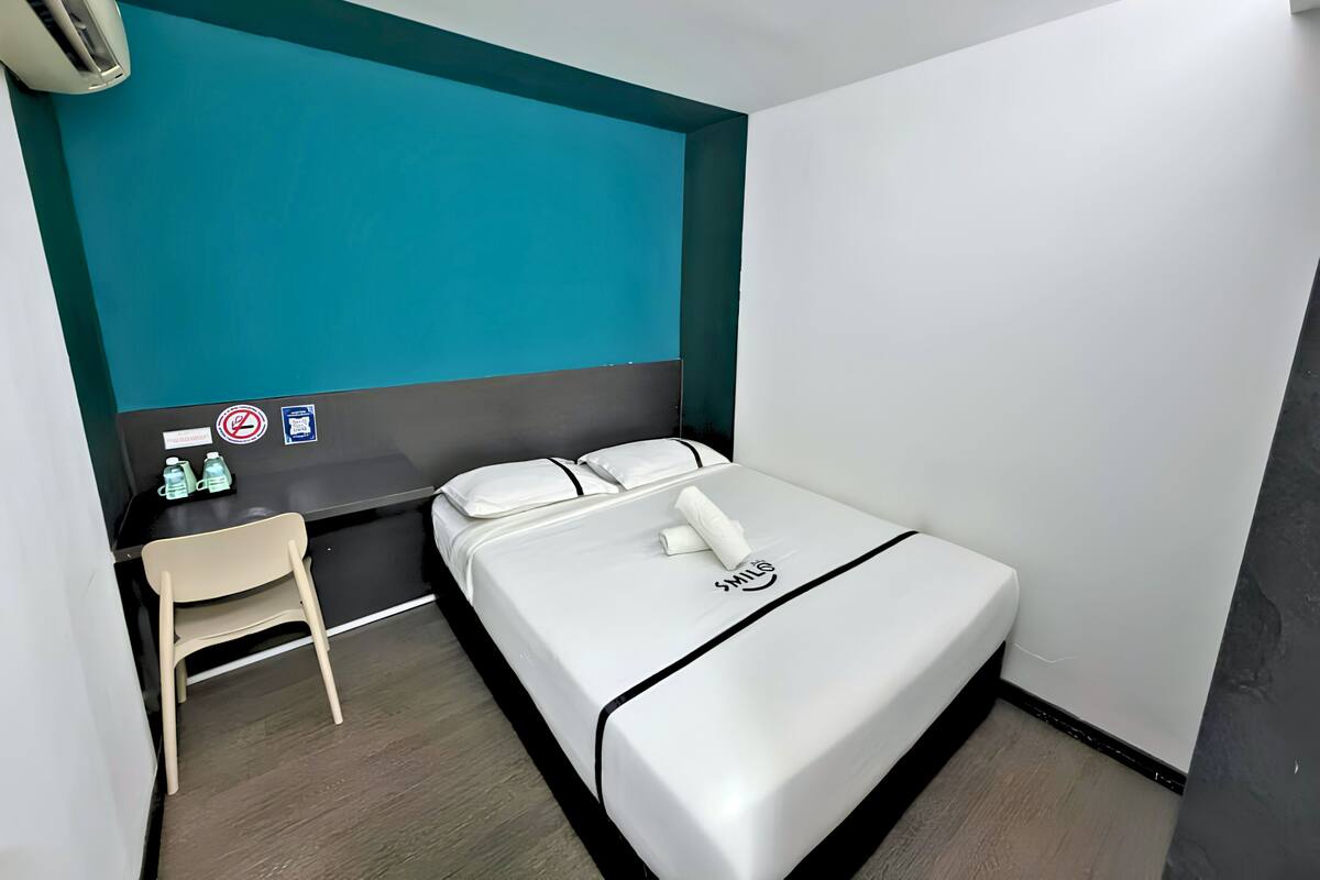 Una camera d'albergo modesta con un letto, una scrivania, una sedia e una parete verde acqua.